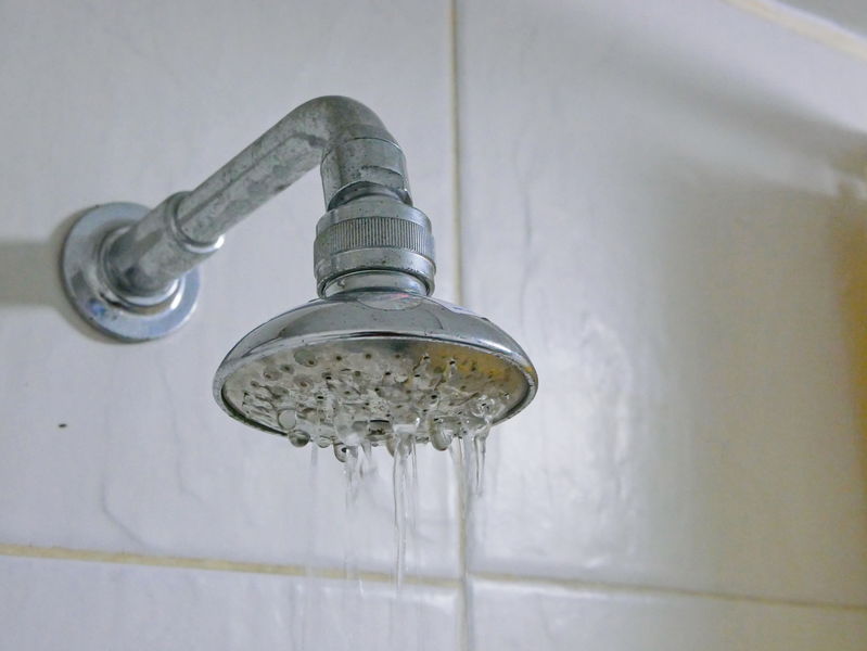 Close up of a partly clogged shower head in a bathroom, causing